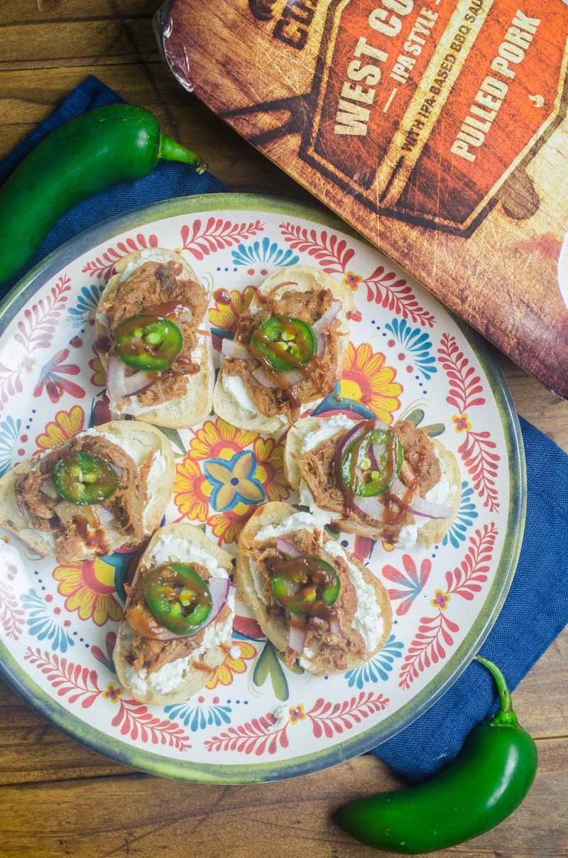 BBQ Pulled Pork Bruschetta is topped with goat cheese, Curly’s RoadTrip Eats West Coast IPA Style Pulled Pork, onions, jalapenos and BBQ sauce. It’s perfect for game day!