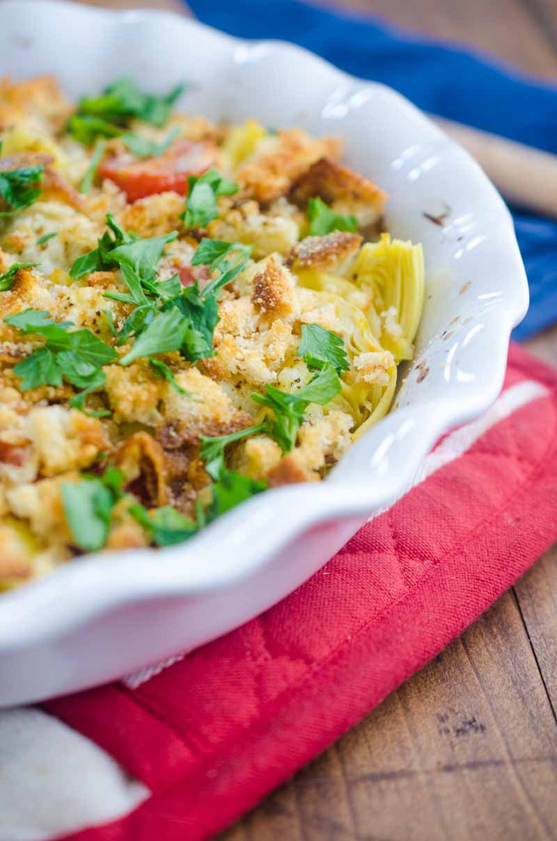 Tomato Artichoke Bake is the perfect side! It's loaded with artichoke hearts, fresh bread crumbs, tomatoes, grated parmesan and then baked until golden.