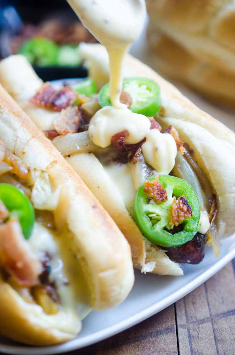 Ultimate cheesy brats are loaded with caramelized onions, cheese sauce, jalapeños and bacon. They are the perfect way to celebrate National Bratwurst day! #ad