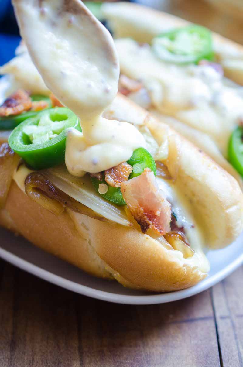 Ultimate cheesy brats are loaded with caramelized onions, cheese sauce, jalapeños and bacon. They are the perfect way to celebrate National Bratwurst day! #ad