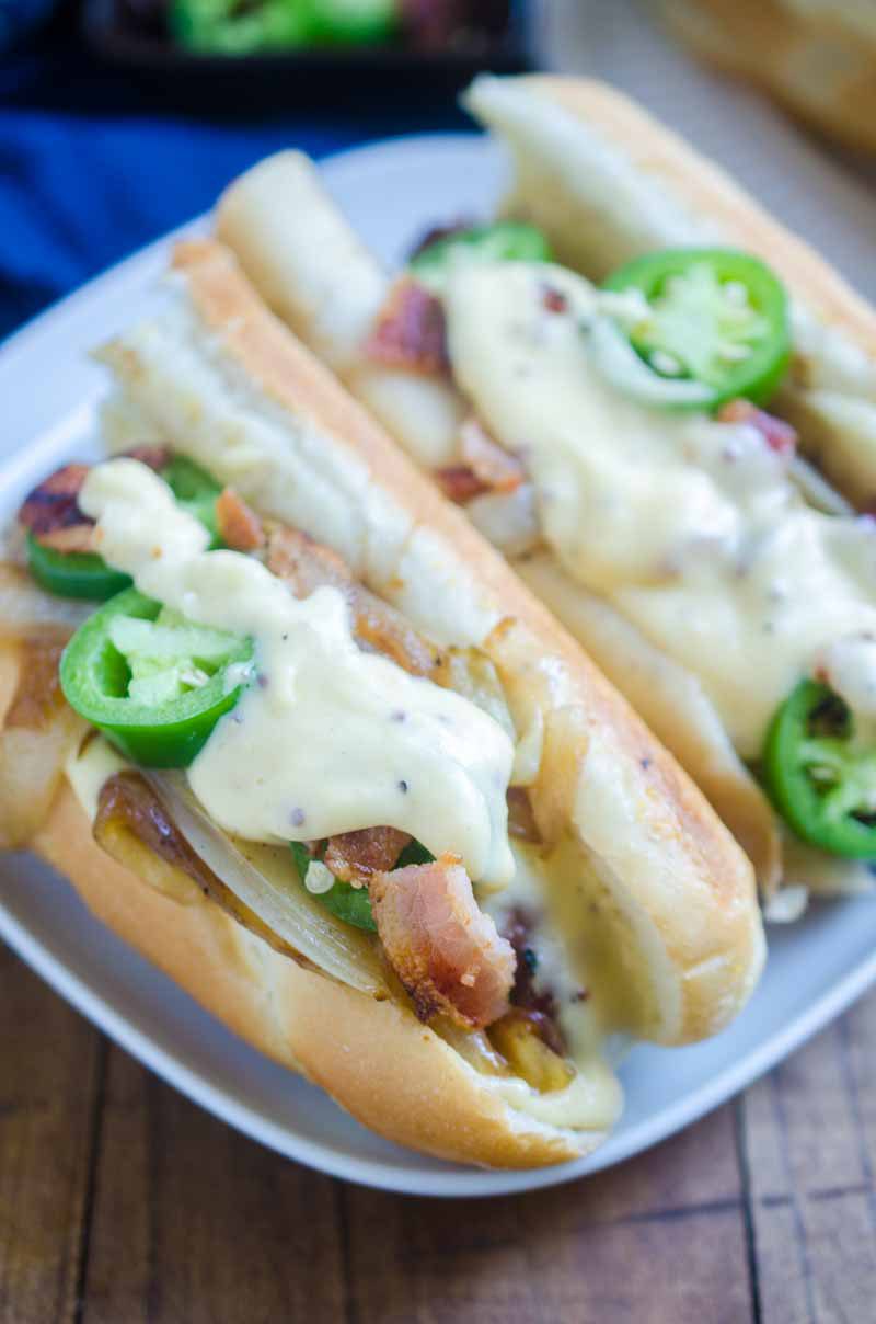 Ultimate cheesy brats are loaded with caramelized onions, cheese sauce, jalapeños and bacon. They are the perfect way to celebrate National Bratwurst day!