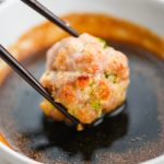 Chopsticks dipping meatball into soy dipping sauce.