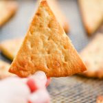 A hand holding a homemade pita chip.