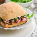 Ribeye steak sandwich on a white plate with arugula.