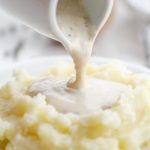 Pouring white country gravy on mashed potatoes.