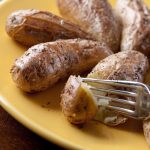 fork cutting roasted potatoes on yellow plate.