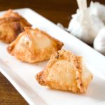 3 Roasted garlic cream cheese wontons on rectangle white plate.