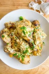 Overhead photo of 40 clove garlic chicken in a white bowl on a wooden cutting board.