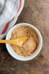 All purpose seasoning blend in a white bowl on cookie sheet with white and red stripped towel.