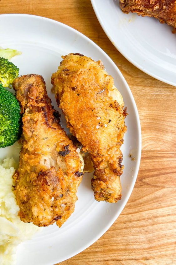 Overhead photo of fried chicken on a white plate with mashed potatoes and broccoli.