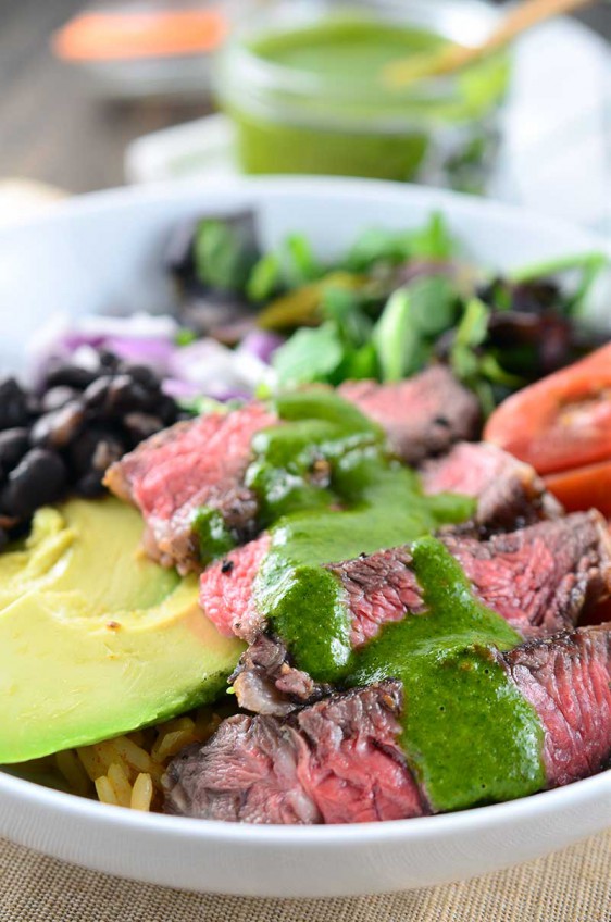 Chimichurri Steak Bowl loaded with sliced ribeye, avocado, tomatoes, red onion, black beans, spanish rice and lettuce then drizzled with chimichurri.