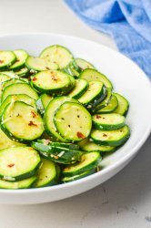 Side angle photo of cold zucchini salad in a white bowl with a blue napkin.