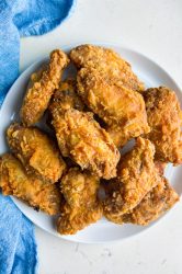 Overhead photo of chicken wings on a white plate with a blue towel.