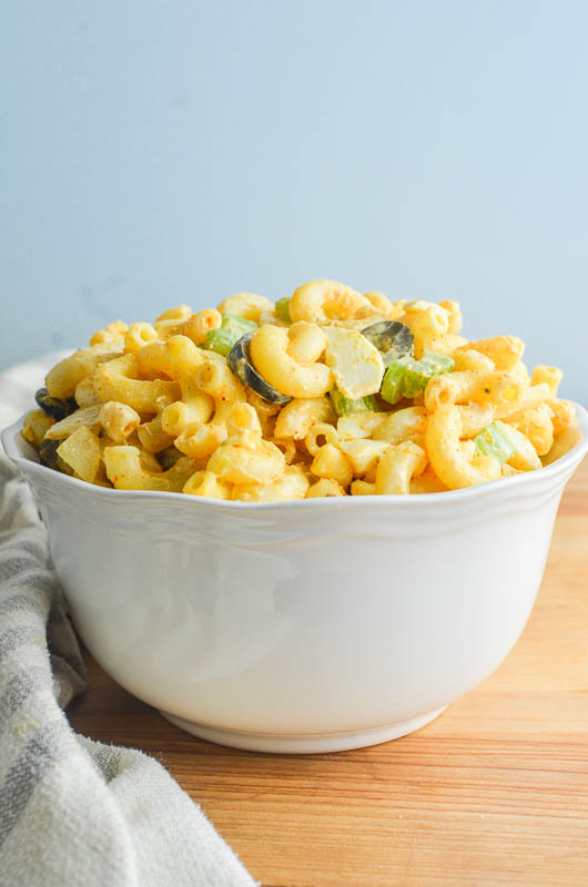 Side angle shot of macaroni salad in a white bowl with a light blue background.