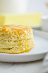 Buttermilk biscuit with a honey drizzle on white plate.