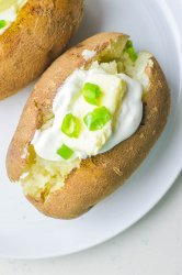 Overhead photo of baked potato on a white plate with sour cream, butter and green onions.