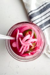Overhead photo of pickled red onions in a glass jar with a fork.