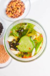 Overhead photo of pickles with crushed red peppers, mustard seeds and peppercorns off to the side.