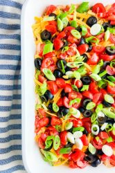 Overhead photo of seven layer dip in a white dish with striped towel.