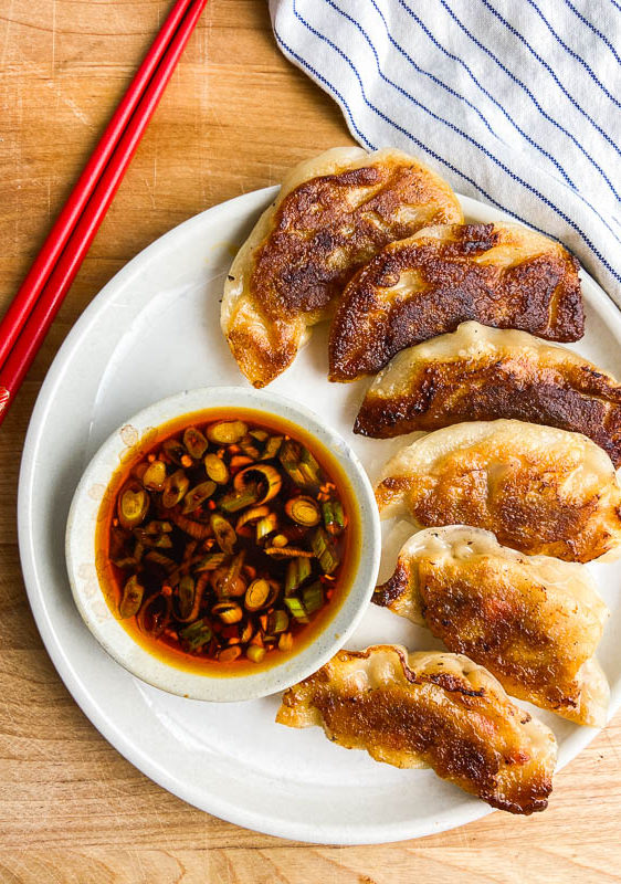Overhead photo of pork potstickers on a white plate with sauce.