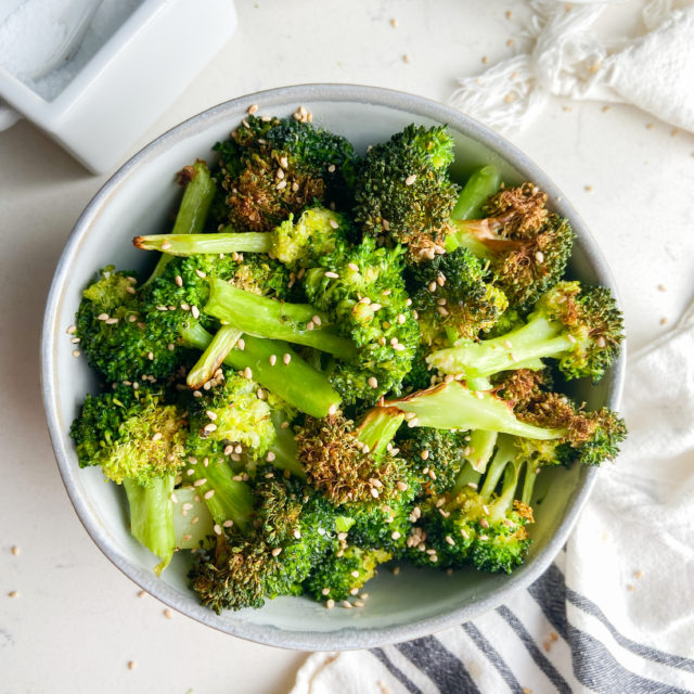 Overhead photo of air fryer broccoli in a bowl with salt, garlic and umami powder.