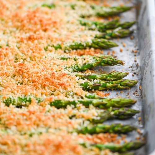 Asparagus on baking dish covered with breadcrumbs.