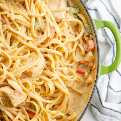 Overhead photo of creamy cajun chicken pasta in a green braising pan.