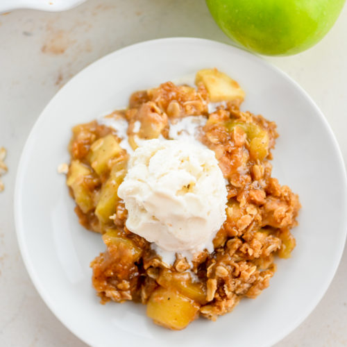 Apple crisp with ice cream on white plate.