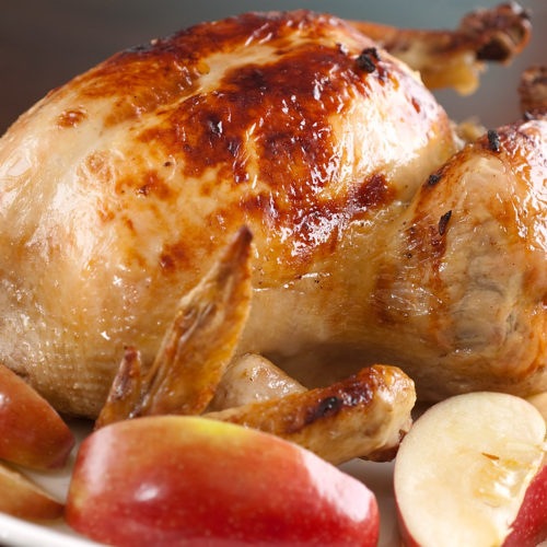 whole roasted chicken on white plate with sliced apples.