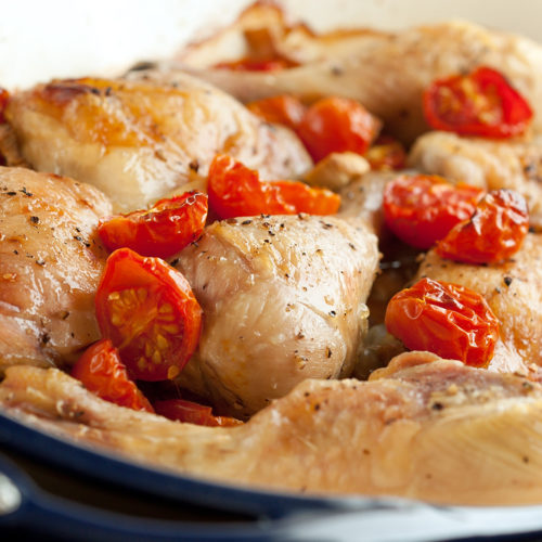Baked chicken with tomatoes in baking dish.