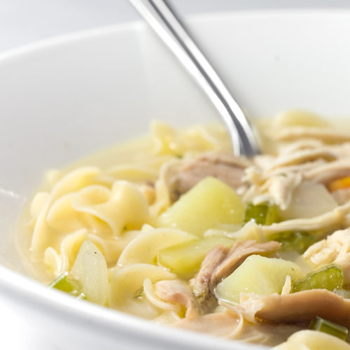 Close up of chicken noodle soup in white bowl.