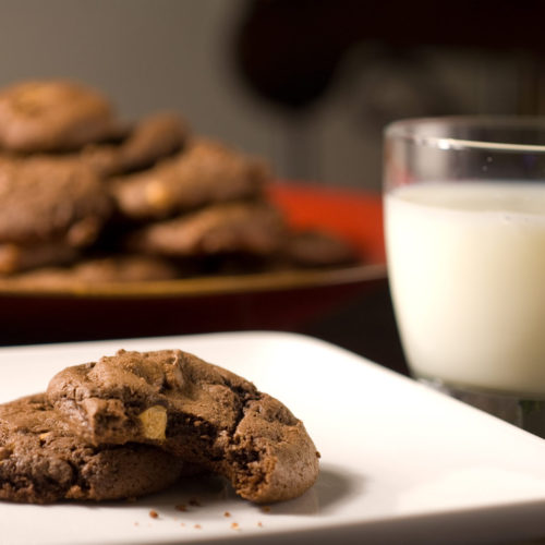 Chocolate butterscotch cookies on white plate with glass of milk.