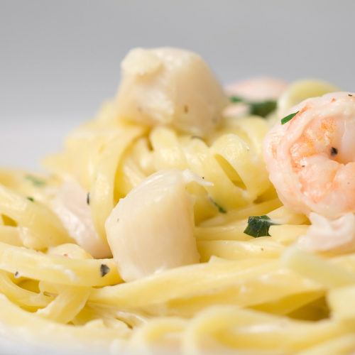 creamy shrimp and scallop pasta in white bowl.