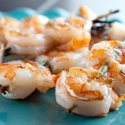 grilled shrimp on rosemary skewers teal plate.