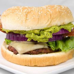 guacamole bacon cheese burger on white plate.