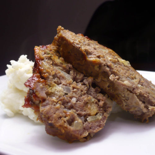 meatloaf on white plate with mashed potatoes.