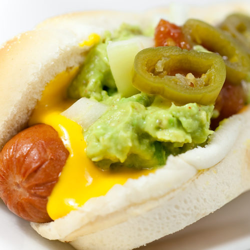 Close up of nacho hot dog on white plate.