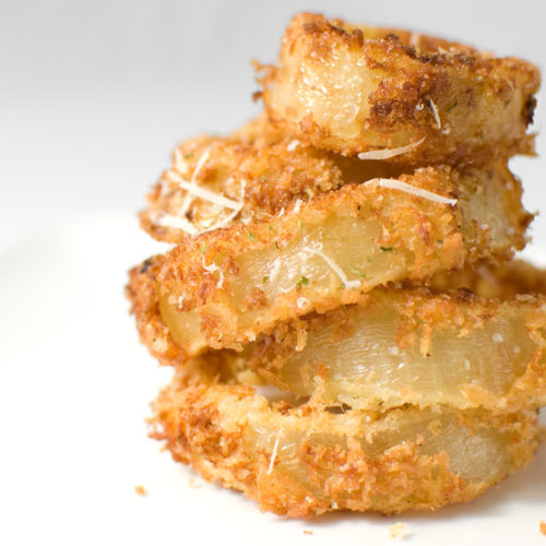 Crispy Parmesan Onion rings in a stack on white plate.