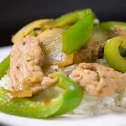 Pork stir fry with peppers and mushrooms on white plate with rice.