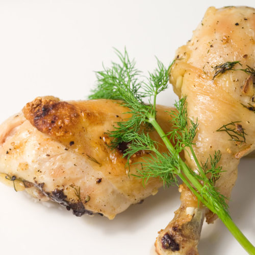 two chicken drumsticks on plate with dill.
