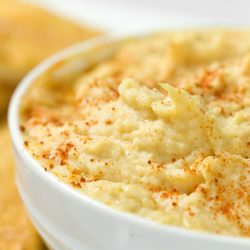 Close up of roasted garlic hummus in white bowl.