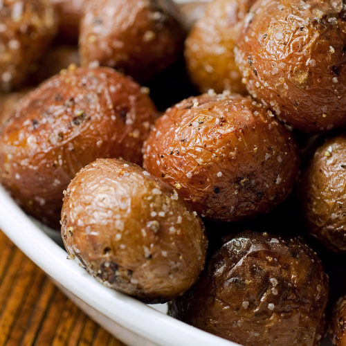 Close up of roasted potatoes with truffle oil in white bowl.