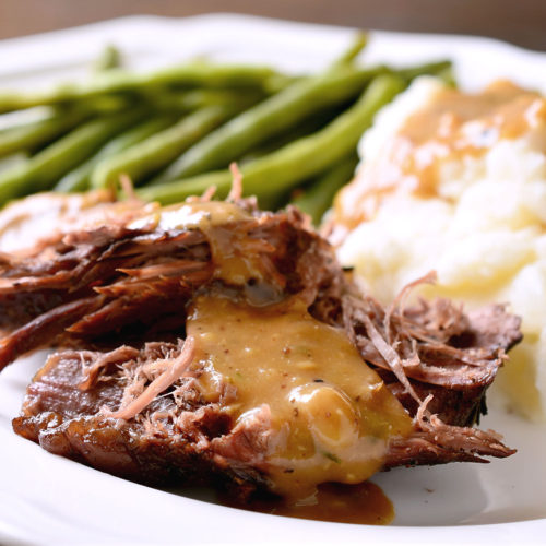 rosemary garlic pot roast on plate with green beans and mashed potatoes.