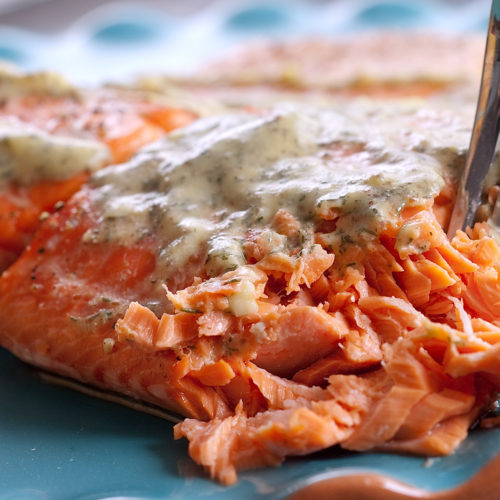 Salmon with mustard dill sauce on teal plate.
