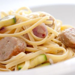 Sausage mushroom and zucchini pasta in white bowl.