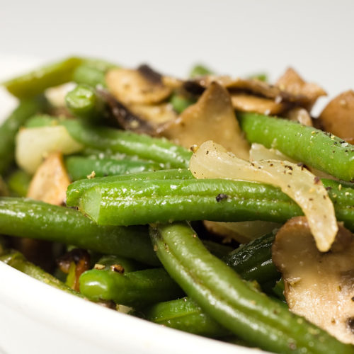 Sauteed green beans with onions and mushrooms in white dish.