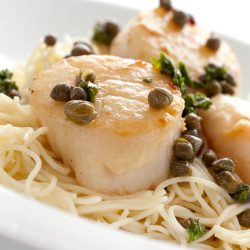 Close up of scallop piccata pasta in white bowl.