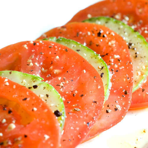 sliced cucumber tomato salad on white plate.