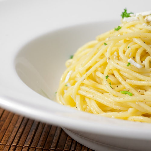 Spaghetti with browned butter and mizithra cheese in white pasta bowl.
