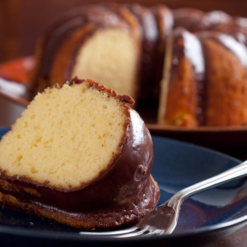slice of yellow cake with chocolate glaze on blue plate with fork.